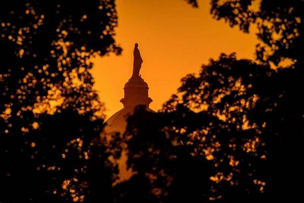 The summer sky is orange and tree branches linger around the outline of the Golden Dome.