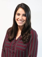 Young woman with dark hair and a bright smile wears a maroon, black, and white striped shirt with a gold necklace.
